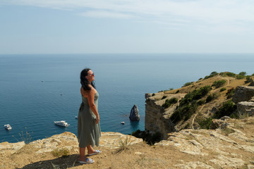 Fototapeta na wymiar A young woman stands on the edge of a cliff and admires the view of the sea.