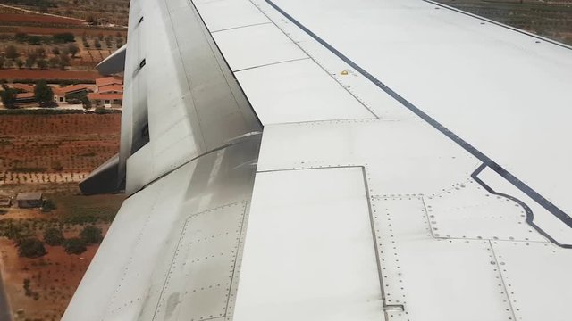 Wing view of aircraft flaps moving during windy landing. Athens International Airport Eleftherios Venizelos day view landing with flap track mechanism spoilers up, ready to increase ground roll drag.
