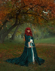 red-haired beauty in search of the victim, the legend of Robin Hood, mysterious lady in green velvet long raincoat with arrows and bow in her hands, fearless girl ready for battle in a foggy forest