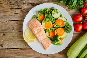 Fototapeta na wymiar Steam salmon and vegetables, Paleo, keto, fodmap diet. White plate on old rustic wooden table, top view, copy space.