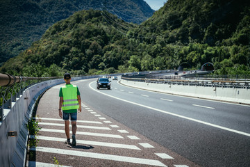 Man in reflective vest arranges a warning triangle, car breakdown on the highway