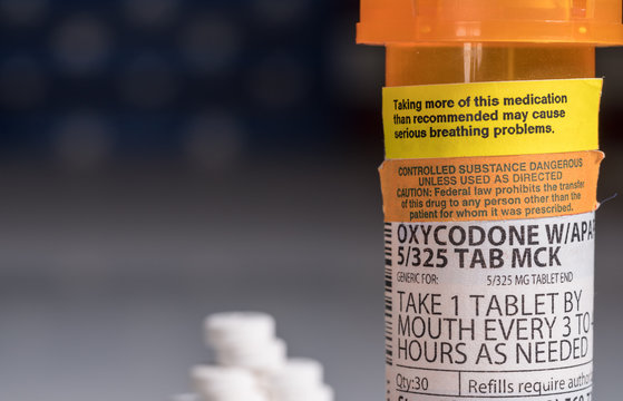 Oxycodone is the generic name for a range of opoid pain killing tablets. Prescription bottle for Oxycodone tablets and pills with USA flag in background