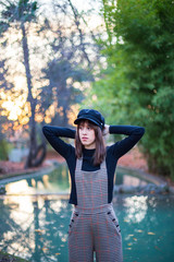Young woman with stylish clothes posing in the green park at sunset