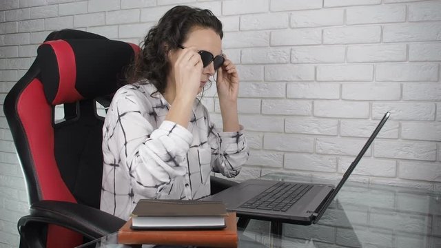 Woman putting on pinhole glasses. The woman at the laptop in the training goggles for the eyes.
