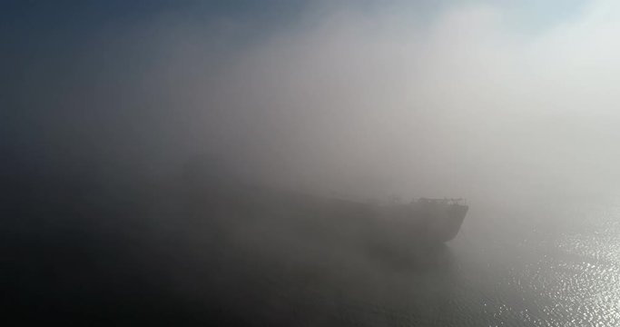 A huge barge on the river Dnipro in the morning fog with a visible silhouette of the buildings and city in the background (shot from the air) in 4K 6