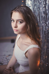 Fototapeta premium delicate and beautiful young girl in white dress on the background of garlands and tinsel