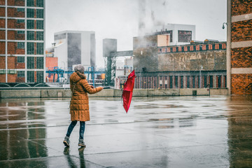 Woman with red umbrella is walking in idustrial city during blizzard