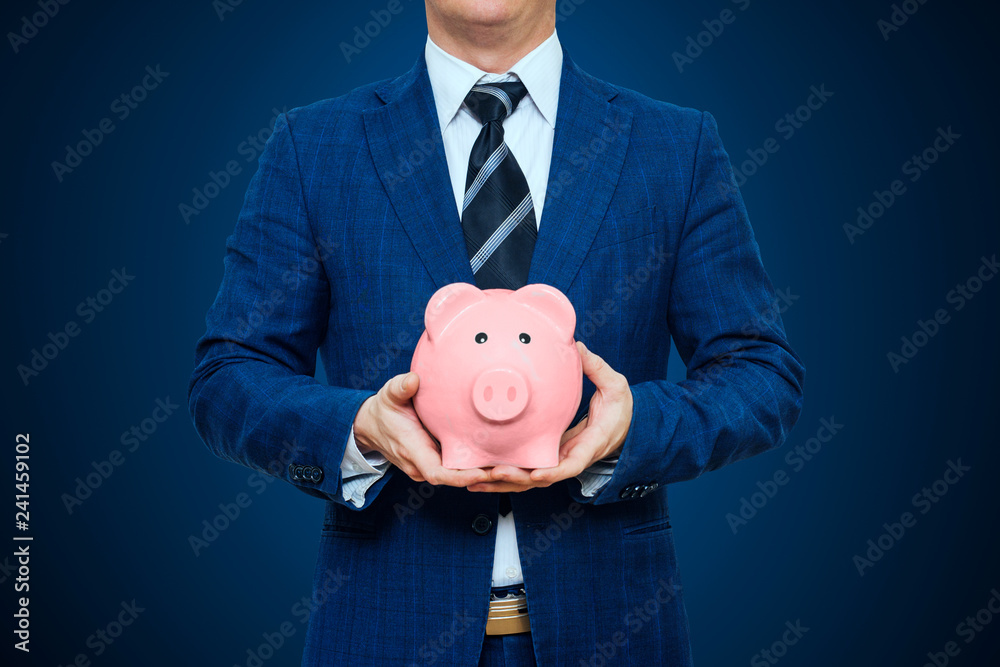 Wall mural businessman in suit is holding piggy bank. businessman holding pig money box. finance savings concep