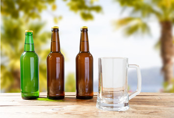 empty goblet and bottles of beer on wooden table on blurred vacation background, craft cider and beer