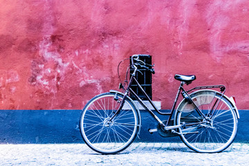 Black bicycle near a red and blue painted wall with a small window