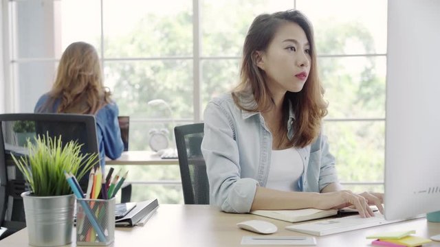 Asian Customer service women using computer answer customer e-mail on desk, female working on laptop while sitting on desk at office. Lifestyle women work at office concept.