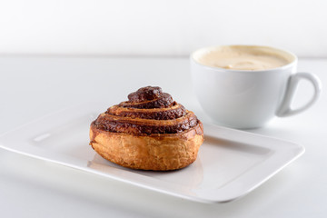 Perfect morning,sweet breakfast and start day.Coffee cup and Cinnamon Danish Swirl-classic buttery bun danish pastry rolled with cinnamon and glazed with sugar on dish on white background.