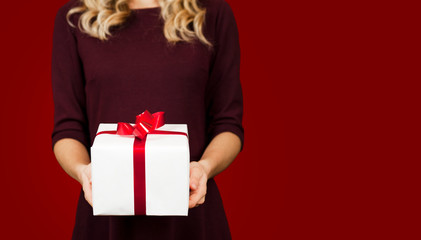 Girl holding a white gift with a red bow close-up on a red background. Valentine's Day concept.