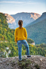 Naklejka premium Young girl with enjoying breathtaking view of the landscape from the top of mountain. Travel concept. Back view.