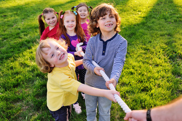 Fototapeta premium a group of small preschool children play a tug of war in the park. Outdoor games, childhood, friendship, leadership, children's day.