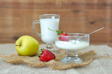 Glass of kefir, apple and strawberry on a wooden table