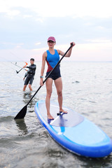 attractive young girl with SUP board on the background of the sea and sunset