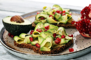 sliced avocado and ripe pomegranates on toast bread with spices and avocado.