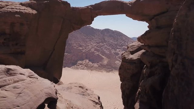 Drone flying under natural arch stone bridge in desert