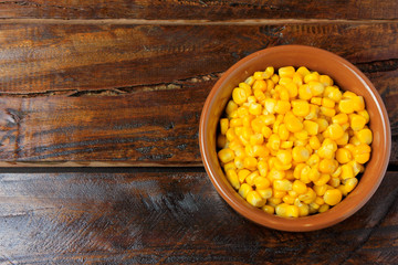 Raw corn kernels inside ceramic pot on rustic wooden table. space for text