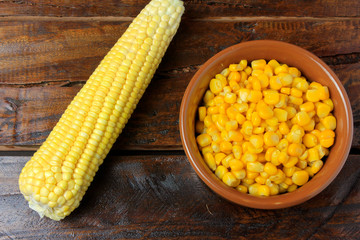 Raw corn kernels inside ceramic bowl on rustic wooden table. space for text