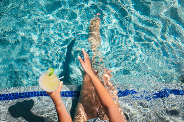 A woman waves her hand across the water while drinking a cocktail in a luxurious pool