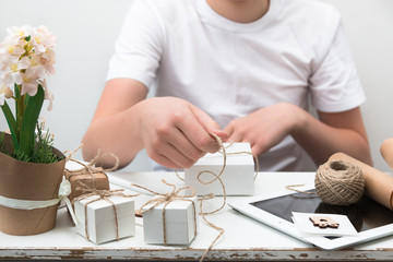 Obraz na płótnie Canvas Teen boy wrapping boxes with gifts for his mother, grandmother and sister to congratulate them on Women's Day on March 8, Mother's Day, Happy Valentine's Day.
