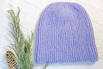 hand-knitted hat in blue, next to a sprig of juniper and a cone on the background of a white jacket hand-knitted