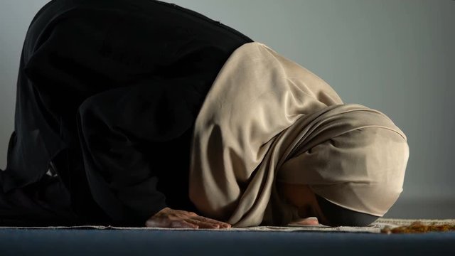 Young female in hijab praying on mat, asking god forgiveness, religious ritual