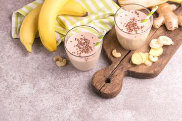 Banana and almond smoothie with ginger and flax seeds in glasses with paper straws on gray marble background. Horizontal view. Copy space
