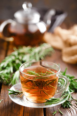 Rosemary tea in glass tea cup on rustic wooden table closeup. Herbal vitamin tea.