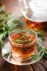 Rosemary tea in glass tea cup on rustic wooden table closeup. Herbal vitamin tea.