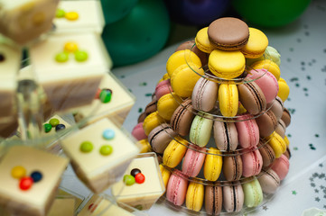 Fototapeta na wymiar Mousse in glasses and colorful french macarons multilevel cake pyramid on plastic dessert stand.