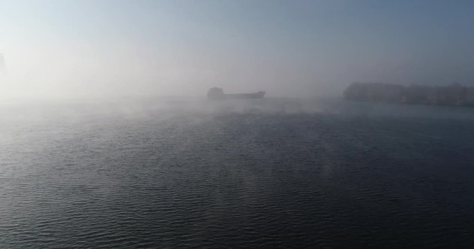 A huge barge on the river Dnipro in the morning fog with a visible silhouette of the buildings and city in the background (shot from the air) in 4K 2