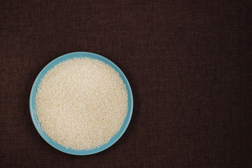 Top view, close up. Blue plate filled with white rice croup. Dark linen background.