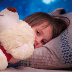 Cute little child girl with toy teddy bear sleeping on bed.
