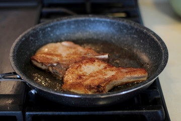 Pork chops frying in a pan on a stove top.
