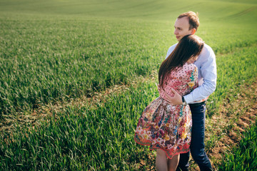 Beautiful young couple gently hugging in sunshine in spring green field. Happy family embracing in green meadow with fresh grass in sunlight. Romantic moments. Valentine day.