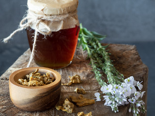 Jar of honey, flowers and wooden bowl and spoon of propolis granules on piece of wood.