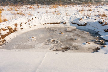 A detailed look at the water runs under the ice in the river. Snow melts from the mountains and flows in the creek