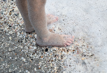 A little girl's sandy feet along a shell-covered beach