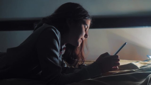 girl teenager and smartphone. little teen hood girl writes a message chatting in social media messenger night evening indoors smartphone on the bed. children technology lifestyle and communication