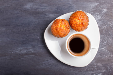 two carrot muffins with cup of coffee on white plate on black wooden background