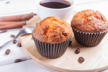 two carrot muffins with cup of coffee on wooden kitchen board on white wooden background