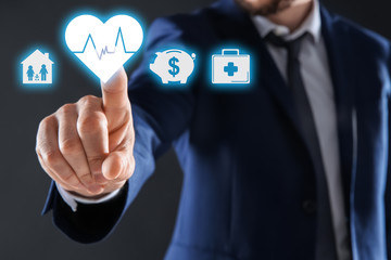 Businessman choosing heart icon on virtual screen against dark background. Life and health insurance