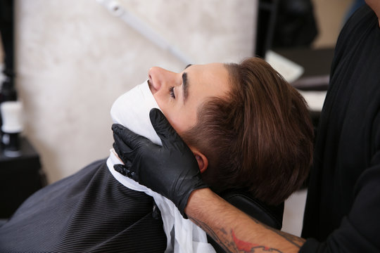 Professional hairdresser using cold towel to calm client's skin after shaving in barbershop