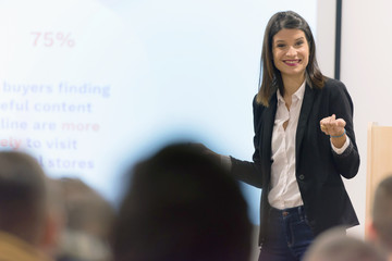 Pretty young businesswoman, teacher or mentor coach speaking to young students in audience at...