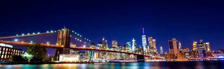 Beautiful Brooklyn Bridge and the illuminated Manhattan's skyline at dusk with dark blue sky and...