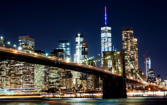 Beautiful Brooklyn Bridge and the illuminated Manhattan's skyline at dusk with dark blue sky and smooth water surface. Picture taken from the Brooklyn district, New York, USA.