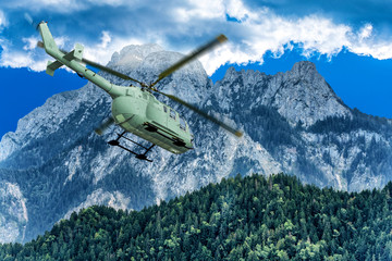 Fototapeta na wymiar Green helicopter on background of high Alps mountains wth green forest under blue cloudy sky.